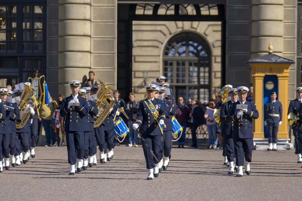 Military band performing in an official ceremony, playing instruments and wearing formal uniforms.