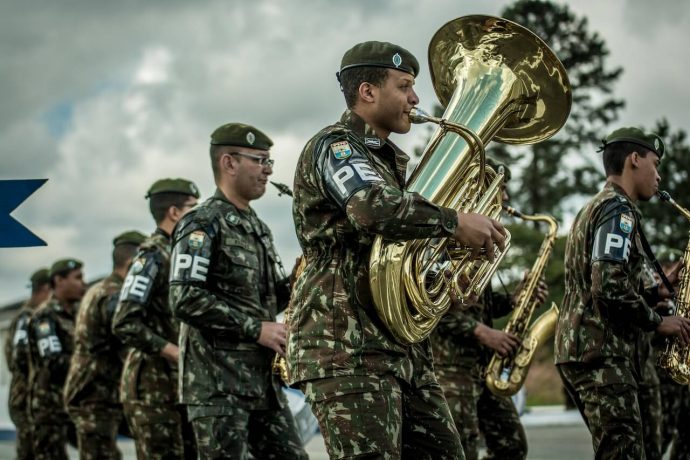 Soldiers in camouflage uniforms playing brass instruments in a musical performance.